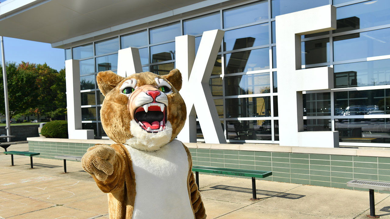 Lake Catholic High School's Cougar mascot standing in front of a Lake sign